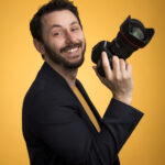 Photographe de Tours pose fièrement avec son appareil en main sur un fond coloré en studio