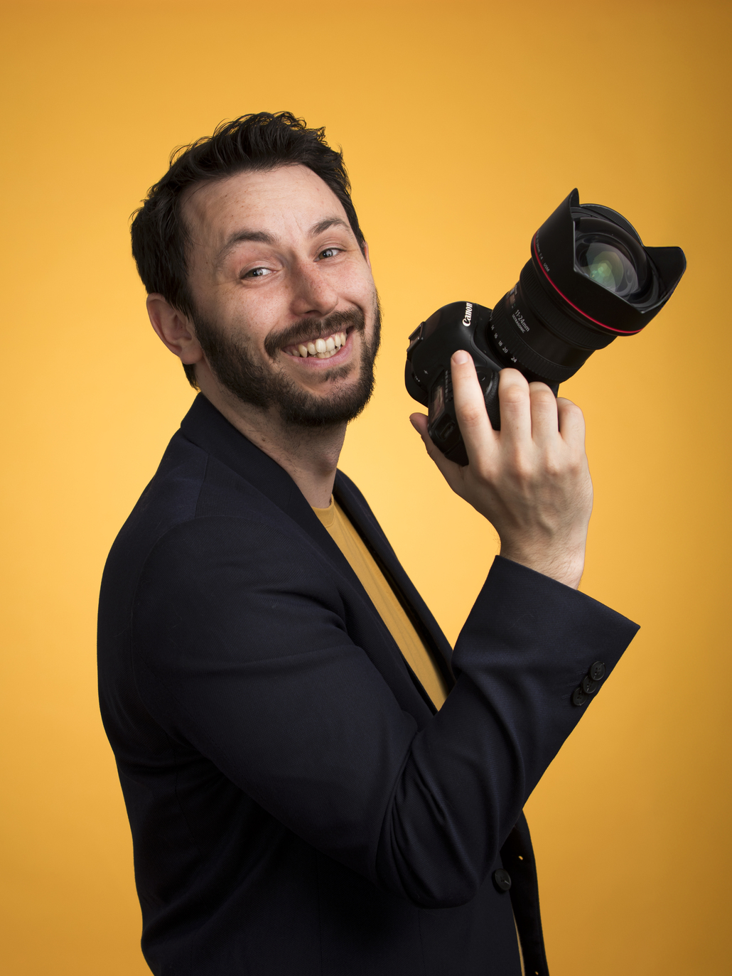 Photographe de Tours pose fièrement avec son appareil en main sur un fond coloré en studio